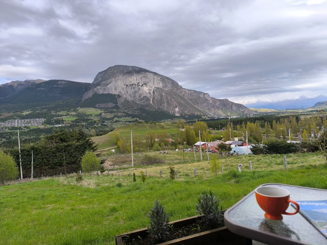 Taza de café sobre la mesa de la terraza, con el cerro y el valle bajo un cielo nublado