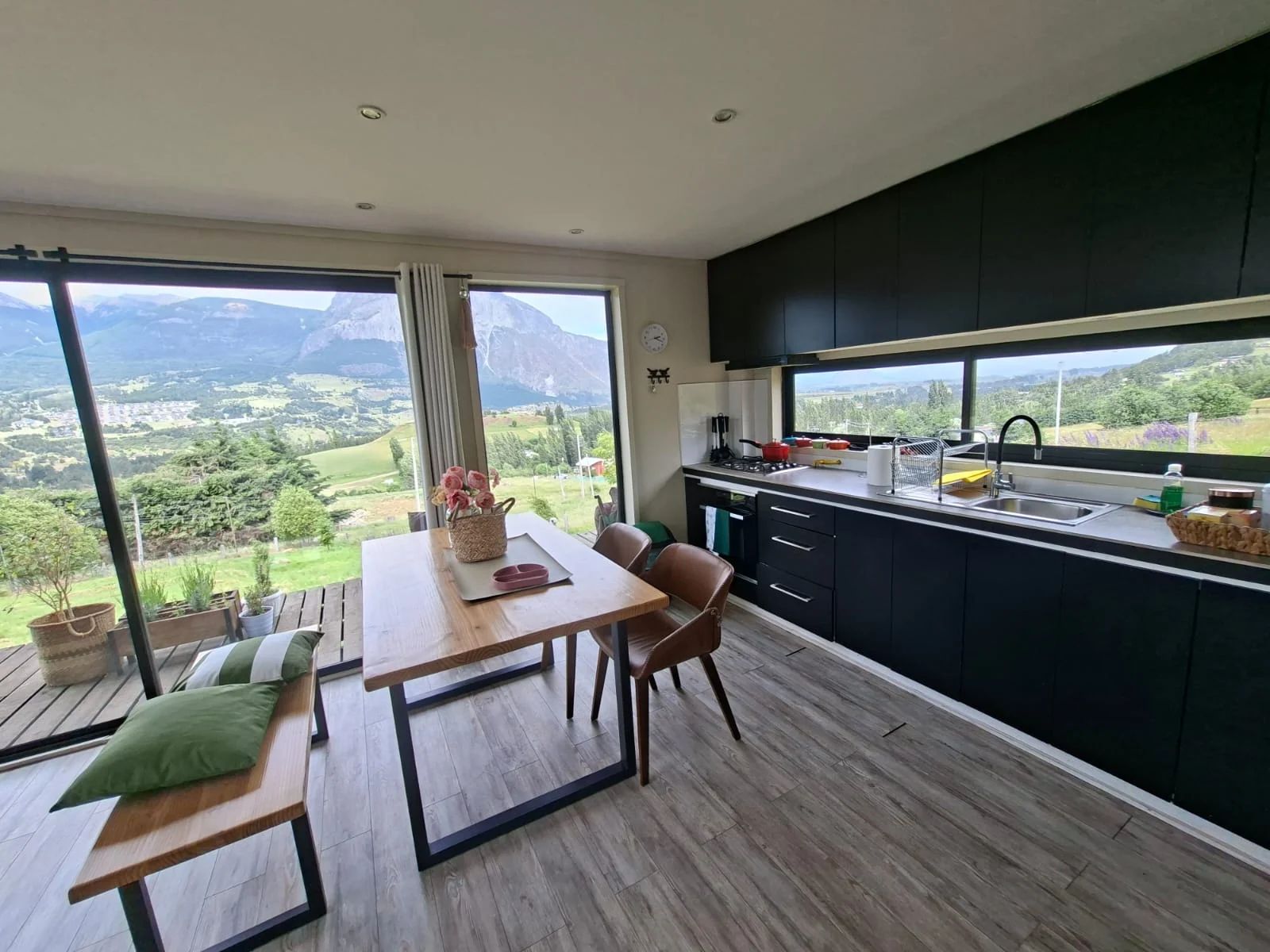 Comedor con banca y cojines junto a la cocina, frente a ventanales con vista al cerro