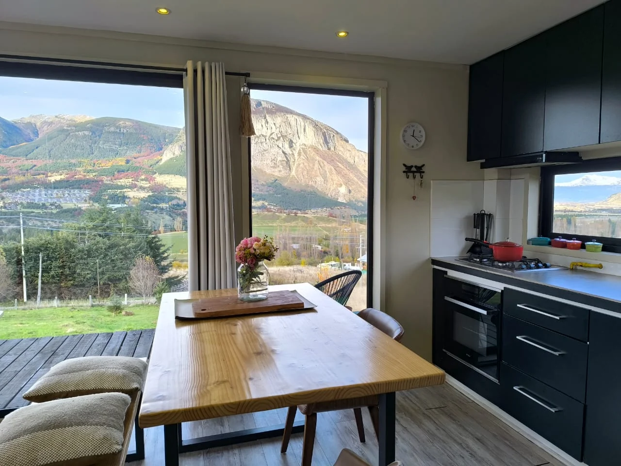 Comedor de madera con flores junto a la cocina, frente al ventanal con vista al cerro