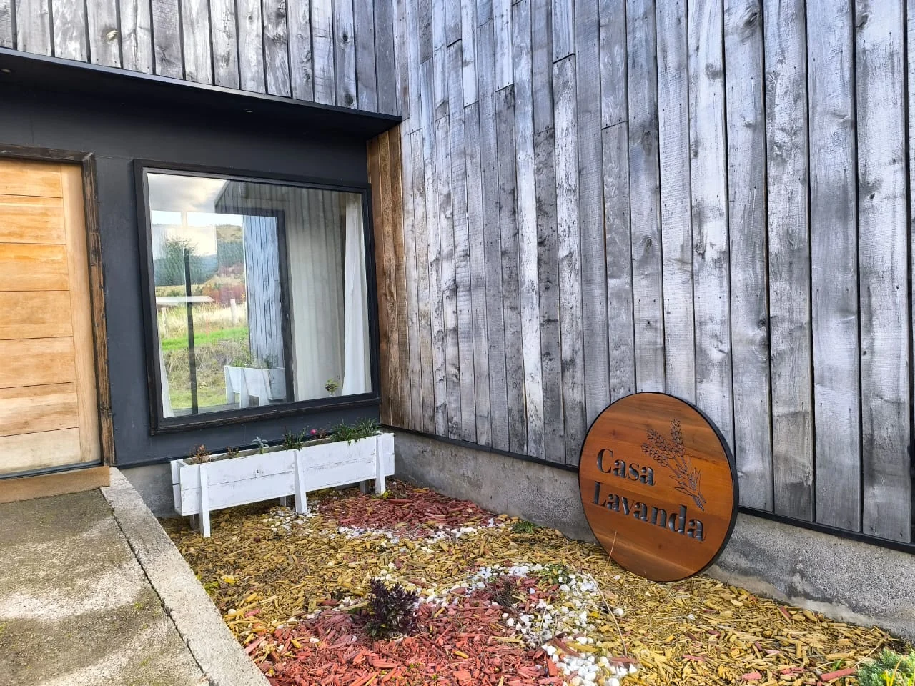 Letrero de madera de Casa Lavanda junto a la ventana y las jardineras de la entrada
