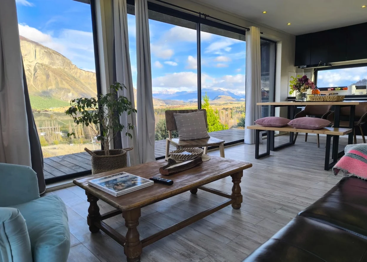 Living de Casa Lavanda con mesa de centro de madera frente a ventanales con vista al cerro y la cordillera