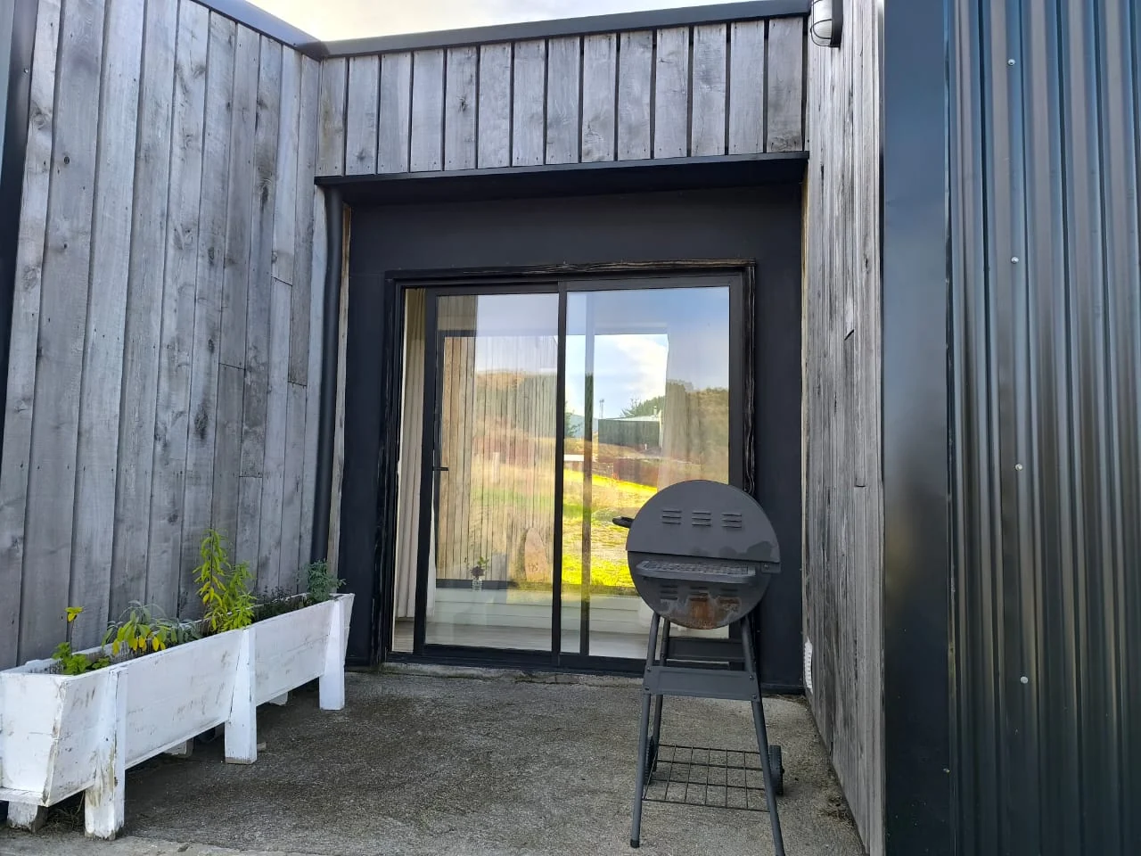 Patio de madera con jardineras blancas y parrilla junto a la puerta de vidrio