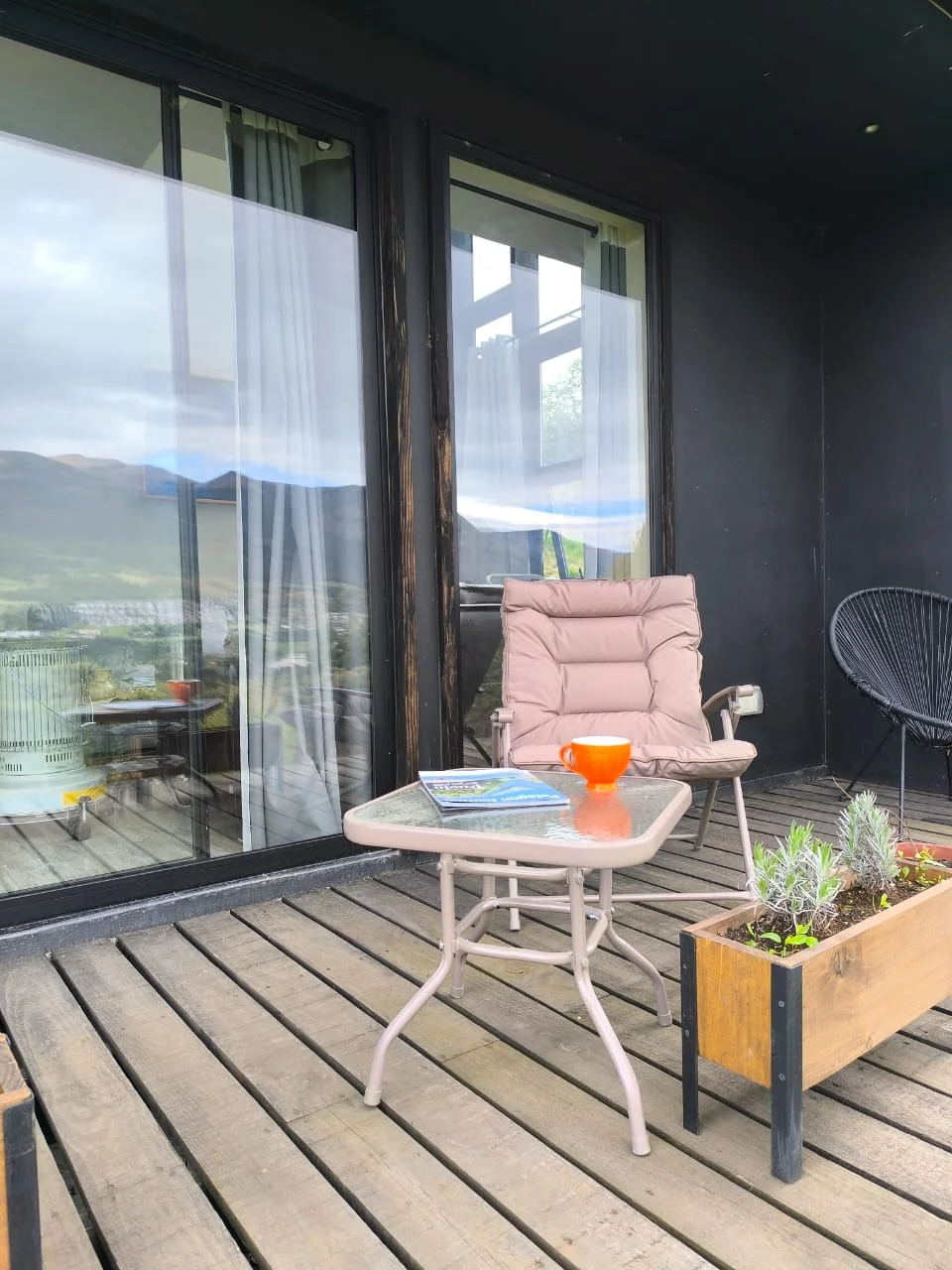 Sillas y mesa en la terraza de madera junto a los ventanales y una jardinera de lavanda
