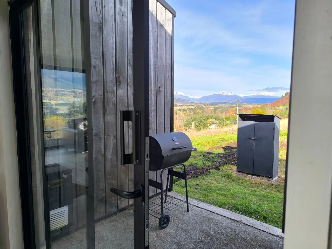 Puerta de vidrio que se abre a la terraza con parrilla y vista a la cordillera